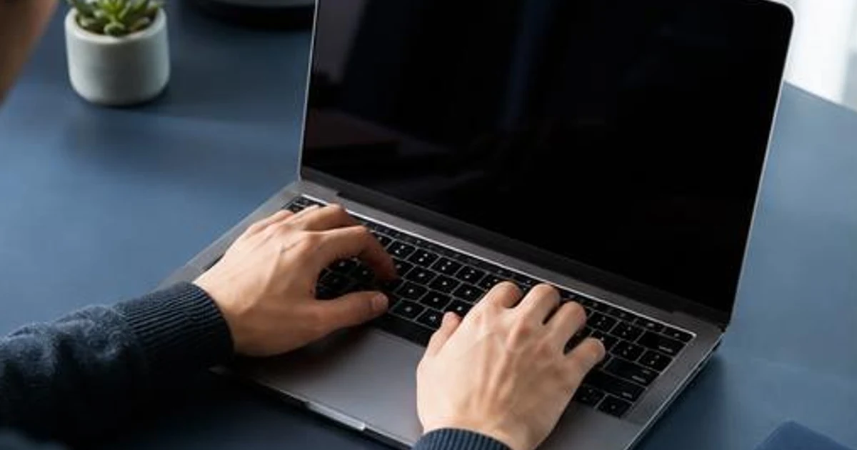 AI-generated editorial illustration, not an actual customer, exposed record or documented incident. AI-generated editorial illustration: hands using a laptop at a blue-gray desk.