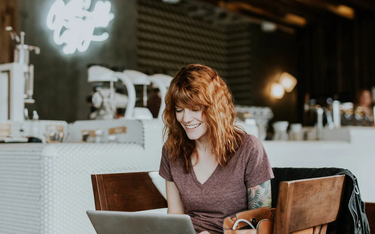 Illustrative photograph of a woman working on her laptop in a naturally lit café.